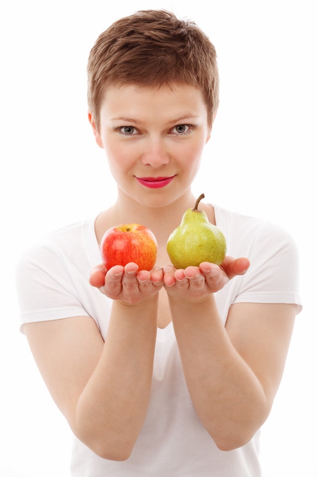 A slim woman holding up an apple and a pear.